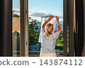 Woman Hanging Laundry on Balcony Viewed Through Open Window 143874112