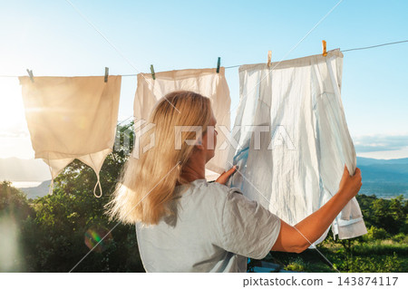 Woman Hanging Fresh Laundry Against Sunny Lake Landscape Woman Hanging Fresh Laundry Against Sunny Lake Landscape 143874117