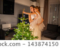 A woman lifts a girl to place a star on top of a Christmas tree. Shared holiday decorating lets a child help with the finishing touches. 143874150