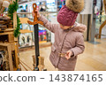 A girl holds a wooden toy sword beside a souvenir stall. Exploring traditional toys turns a shopping trip into a playful childhood experience. 143874165