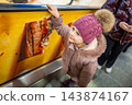 A girl in a winter coat holds an escalator handrail in a shopping mall. Travelling between floors is part of an everyday shopping outing with a child. 143874167