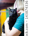 Young person holding black cat with bright green eyes in colorful indoor setting close up portrait showing cat facing camera and emotional bond between pet and owner 143874336
