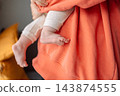Close up of tiny baby feet and legs in mother arms wrapped in soft coral orange blanket 143874555