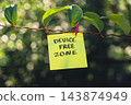 Paper note with DEVICE FREE ZONE message against green leafy background. Suitable for digital detox, screen-free lifestyle technology break mindfulness. 143874949