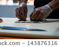 Gloved hands shape a sushi roll on a white board as a sharp Japanese knife rests nearby in a Maldives resort kitchen, soft warm light highlights rice and blade. 143876316