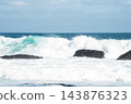 Turbulent white ocean waves break and surge around dark rocky formations along the Atlantic coast in Cape Town, South Africa under a bright daytime sky. 143876323
