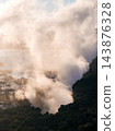Aerial view shows Victoria Falls at sunset as mist surges above the gorge on the Zimbabwe Zambia border, warm light illuminates spray, dark rainforest lines the cliff edge. 143876328