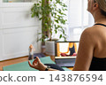 Back view of serene middle aged woman meditating in lotus position with closed eyes on a yoga mat during an online class. Concept of mental health, mindfulness and stress relief. 143876594