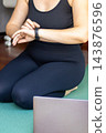 Close up of a woman hands checking a smart watch fitness tracker before starting a home yoga workout on a green mat. Technology, healthcare and sports tracking concept. 143876596