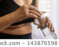 Close up of a woman hands holding a reusable glass water bottle with a charcoal filter during a home fitness workout. Concept of healthy hydration and eco friendly lifestyle. 143876598