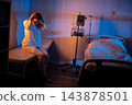Woman exhibits stress near hospital bed. Female patient displays exhaustion by medical equipment. Tired woman shows distress alongside hospital monitor and IV stand 143878501