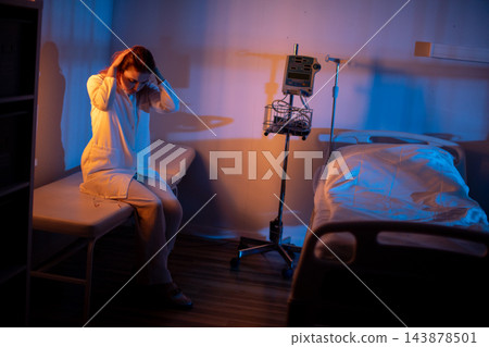 Woman exhibits stress near hospital bed. Female patient displays exhaustion by medical equipment. Tired woman shows distress alongside hospital monitor and IV stand 143878501