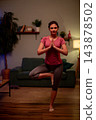 Woman balancing in tree pose near sofa, palms pressed, steady gaze and quiet concentration, living room practice for stability office manager cultivating focus between tasks 143878502