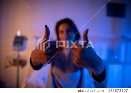 Patient shows confident positive attitude. Smiling individual exhibiting hope and recovery signs. Person with cheerful expression giving thumbs up in healthcare setting 143878507
