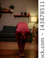 Gentle stretch at home. Maintaining comfort with calming evening stretch routine. Engaging in soothing selfcare stretch on wooden flooring by sofa in warm light 143878511