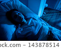 Patient lying awake in hospital bed, closeup portrait reveals weary eyes and tense expression, IV line and gown visible, wakefulness and uncertainty captured in stillness 143878514