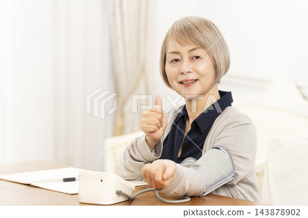 一位老婦人在客廳量血壓時面帶微笑。 一位老婦人在客廳量血壓時面帶微笑。 143878902