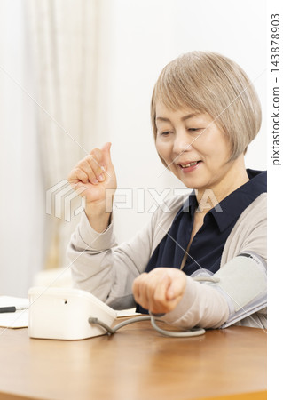 一位老婦人在客廳量血壓時面帶微笑。 一位老婦人在客廳量血壓時面帶微笑。 143878903
