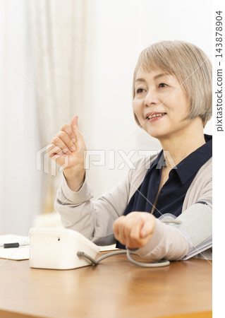一位老婦人在客廳量血壓時面帶微笑。 一位老婦人在客廳量血壓時面帶微笑。 143878904