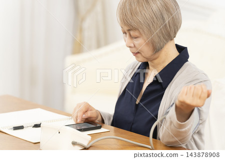一位老婦人在客廳量血壓時面帶微笑。 143878908