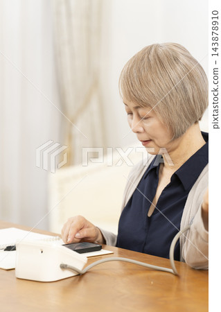 一位老婦人在客廳量血壓時面帶微笑。 一位老婦人在客廳量血壓時面帶微笑。 143878910
