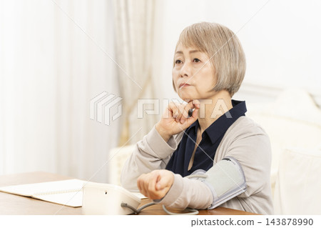一位老年婦女在客廳量完血壓後情緒低落。 一位老年婦女在客廳量完血壓後情緒低落。 143878990