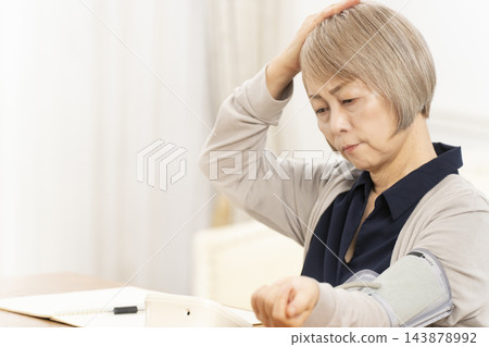 一位老年婦女在客廳量完血壓後情緒低落。 一位老年婦女在客廳量完血壓後情緒低落。 143878992