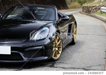 一輛黑色保時捷Boxster Spyder跑車靜靜地停在蜿蜒的道路上。 143880357