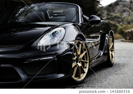 一輛黑色保時捷Boxster Spyder跑車靜靜地停在蜿蜒的道路上。 一輛黑色保時捷Boxster Spyder跑車靜靜地停在蜿蜒的道路上。 143880358