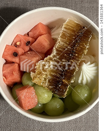 Swirled yogurt ice cream dessert served in a cup, smooth creamy texture with glossy surface, topped with fresh fruit pieces, highlighting its refreshing and inviting appearance in detail 143881364