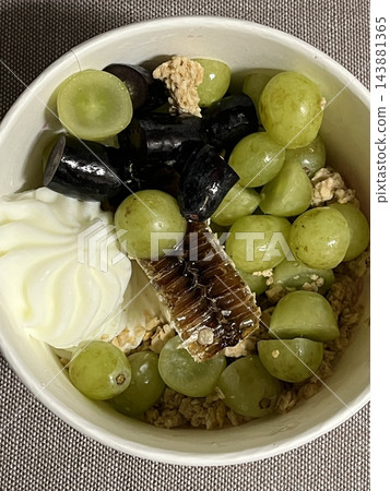 Swirled yogurt ice cream dessert served in a cup, smooth creamy texture with glossy surface, topped with fresh fruit pieces, highlighting its refreshing and inviting appearance in detail 143881365