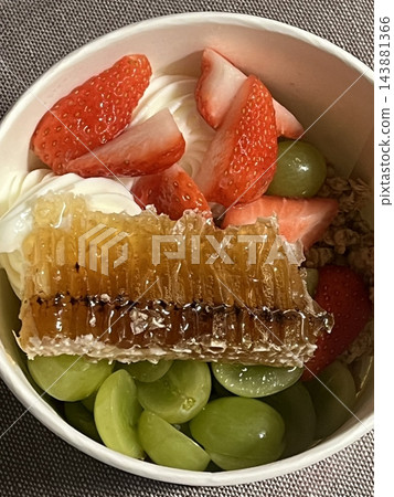 Swirled yogurt ice cream dessert served in a cup, smooth creamy texture with glossy surface, topped with fresh fruit pieces, highlighting its refreshing and inviting appearance in detail 143881366