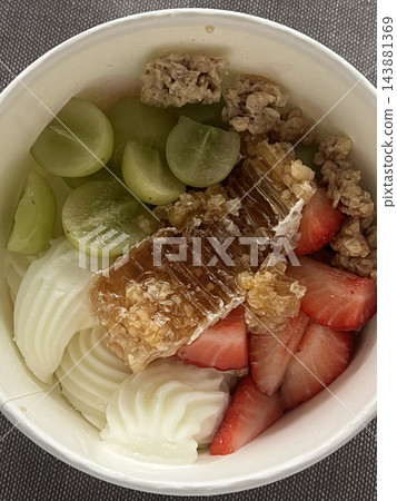 Swirled yogurt ice cream dessert served in a cup, smooth creamy texture with glossy surface, topped with fresh fruit pieces, highlighting its refreshing and inviting appearance in detail 143881369