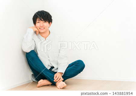 一位年輕男子坐在地板上，以白牆為背景，面帶微笑。 143881954