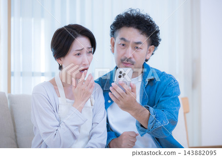 一對中年夫婦在客廳看著智慧型手機螢幕,突然得知利率上升、儲蓄減少和家庭財務狀況惡化等新聞,他們的生活方式令人震驚。 一對中年夫婦在客廳看著智慧型手機螢幕,突然得知利率上升、儲蓄減少和家庭財務狀況惡化等新聞,他們的生活方式令人震驚。 143882095