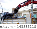 An excavator bucket scooping up broken concrete debris into a dump truck at a road construction site. 143886118
