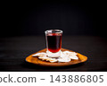 Dark red beverage in a clear glass surrounded by communion wafers on a wooden plate, creating a simple Christian still life for worship, prayer, faith, sacred remembrance, and reflection. 143886805