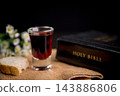 Dark red beverage with sliced bread, white flowers, and a closed religious book on rustic fabric, creating a peaceful still life for faith, prayer, remembrance, worship, and spiritual reflection. 143886806