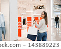 Smiling Woman Walks Away Looking Back with Bags in Shopping Center 143889223
