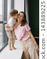 Toddler Boy Kissing His Smiling Mother on the Cheek at Home 143889225