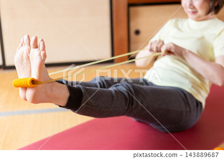 中老年女性在日式房間使用阻力帶進行肌力訓練。 143889687