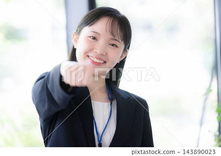 一位二十出頭的日本年輕女性,身穿西裝,戴著員工證,直視鏡頭,擺出勝利的姿勢並揮拳。 一位二十出頭的日本年輕女性,身穿西裝,戴著員工證,直視鏡頭,擺出勝利的姿勢並揮拳。 143890023