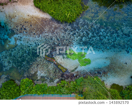 Blue Eye Albania spring forms vivid turquoise pool among dense greenery and pale gravel. Aerial perspective reveals submerged stones beneath transparent water in this tranquil natural setting. Blue Eye Albania spring forms vivid turquoise pool among dense greenery and pale gravel. Aerial perspective reveals submerged stones beneath transparent water in this tranquil natural setting. 143892570