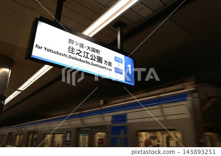 大阪地鐵四橋線西梅田車站的乘客資訊指示牌和一列即將出發的地鐵列車。 143893251