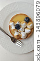 Round fruit tart with glossy yellow filling, blueberries, toasted meringue kisses, and fork on a white textured plate viewed from above, with circular crust and sweet baked pastry 143896079