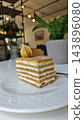 Layered vanilla cream cake slice with golden sponge, textured topping, and dried fruit garnish on a white ceramic plate in a softly lit restaurant interior 143896080
