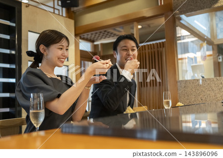 一對四十多歲的男女在吧台座位上吃壽司。 一對四十多歲的男女在吧台座位上吃壽司。 143896096