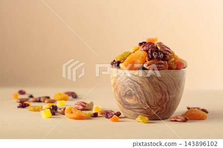 Assorted nuts and dried fruits in wooden bowl on a beige background. Assorted nuts and dried fruits in wooden bowl on a beige background. 143896102