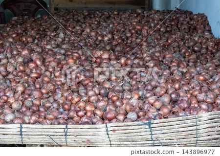 Massive pile of fresh red onions stored in a bamboo container. Raw onion bulbs stacked for wholesale market sale in rural storage setup. 143896977