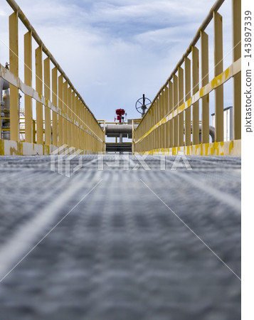 Low angle perspective view of steel grating walkway and yellow safety railings at an industrial plant. Low angle perspective view of steel grating walkway and yellow safety railings at an industrial plant. 143897339